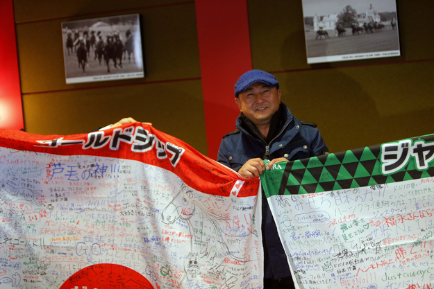 Naosuke Sugai, trainer of Gold Ship, holds flags signed by Japanese fans at a press conference in Chantilly on Oct. 1. Photo: AP Photo/Thibault Camus.