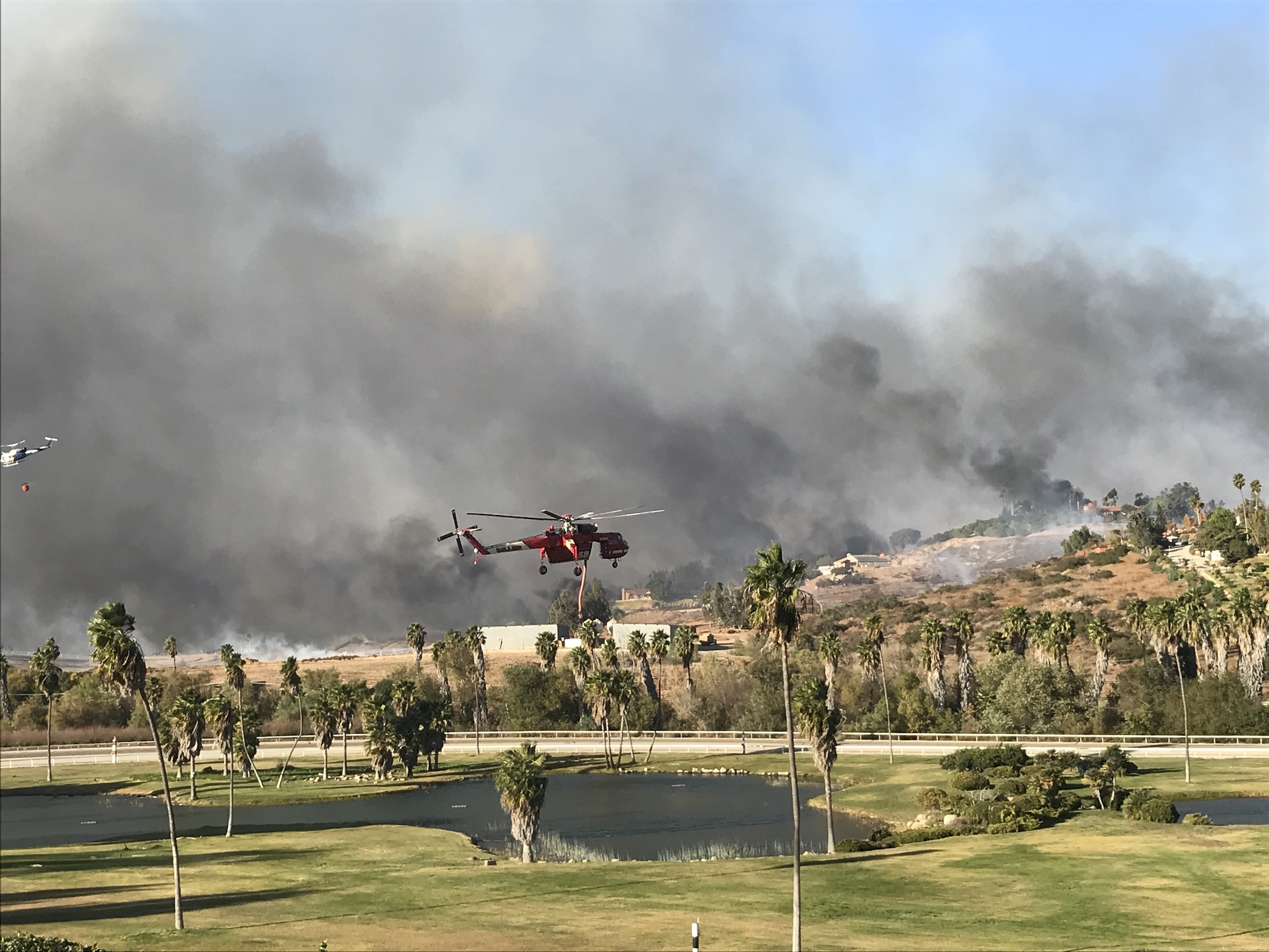 A helicopter arrives to suck water from the ponds at the Trifecta Equine Athletic Center, which is then taken to douse the raging wildfire